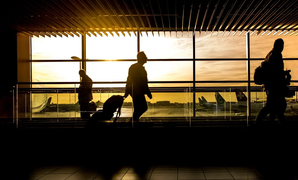Silhuetas de viajantes com malas no saguão de um aeroporto, contra a janela ao pôr do sol